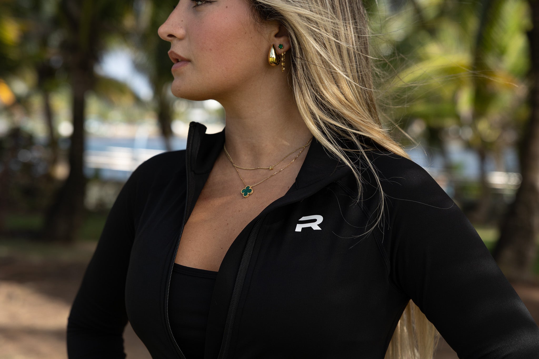 Woman wearing a black jacket with a logo, standing outdoors with blurred background